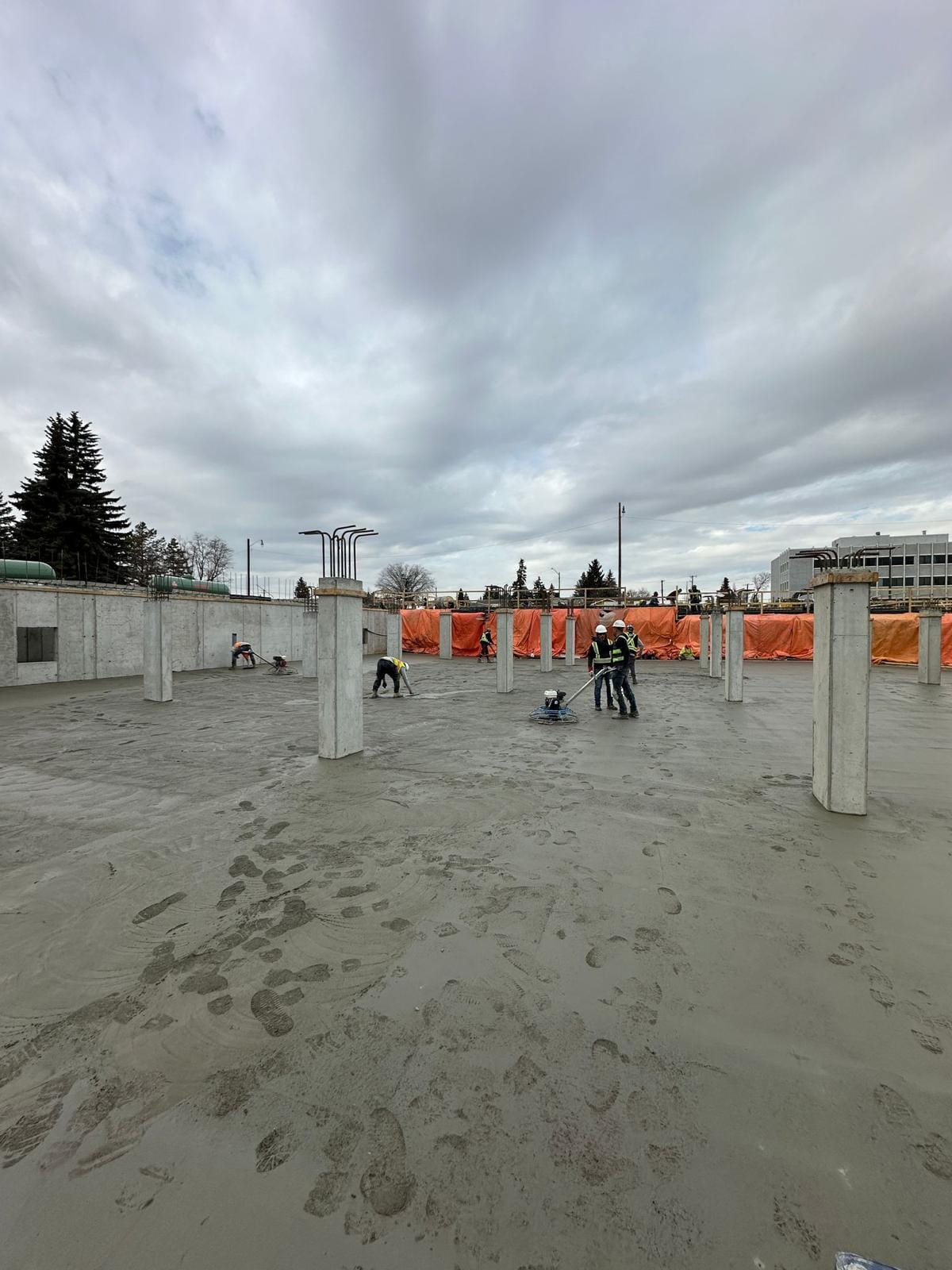 Crew finishing a large poured concrete slab with a power trowel between structural columns
