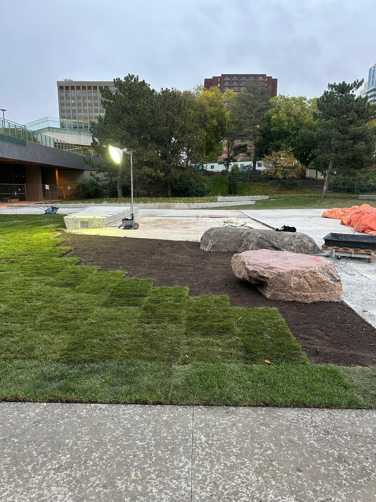 New sod, feature boulders and a concrete plaza under work lights at dusk
