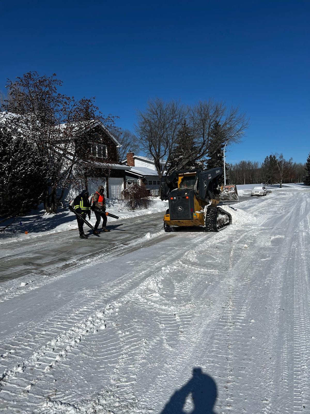 Snow removal crew and skid steer clearing a residential street on a bright winter day in Edmonton